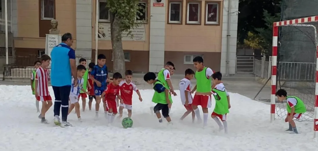 Karla kaplı sahada top oynayan akademi öğrencileri ve antrenör